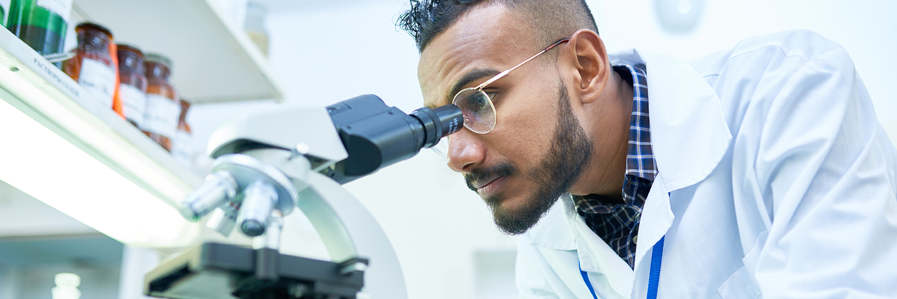 Male scientist in lab looking through microscope 